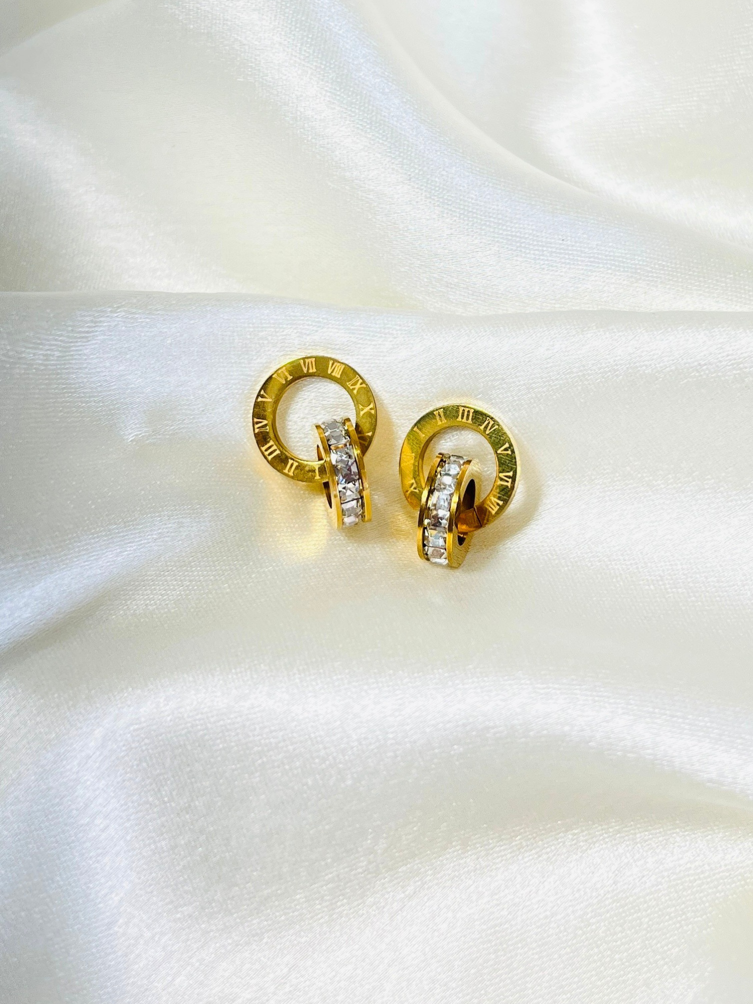 Pair of gold Roman crystal earrings displayed on a white satin background showcasing intricate detailing.