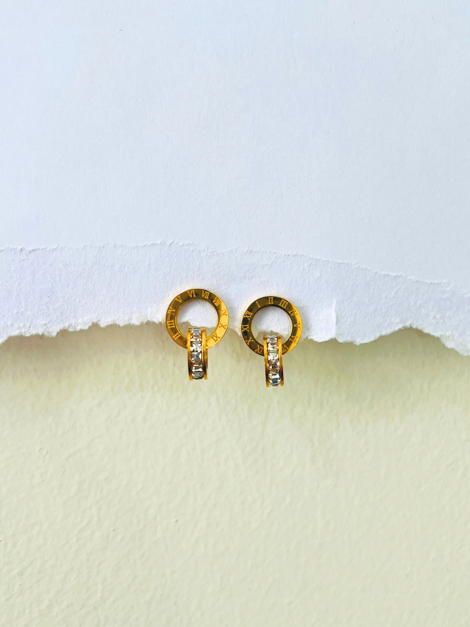 Simple gold earrings design with Roman-inspired crystal detailing placed on a clean white background.