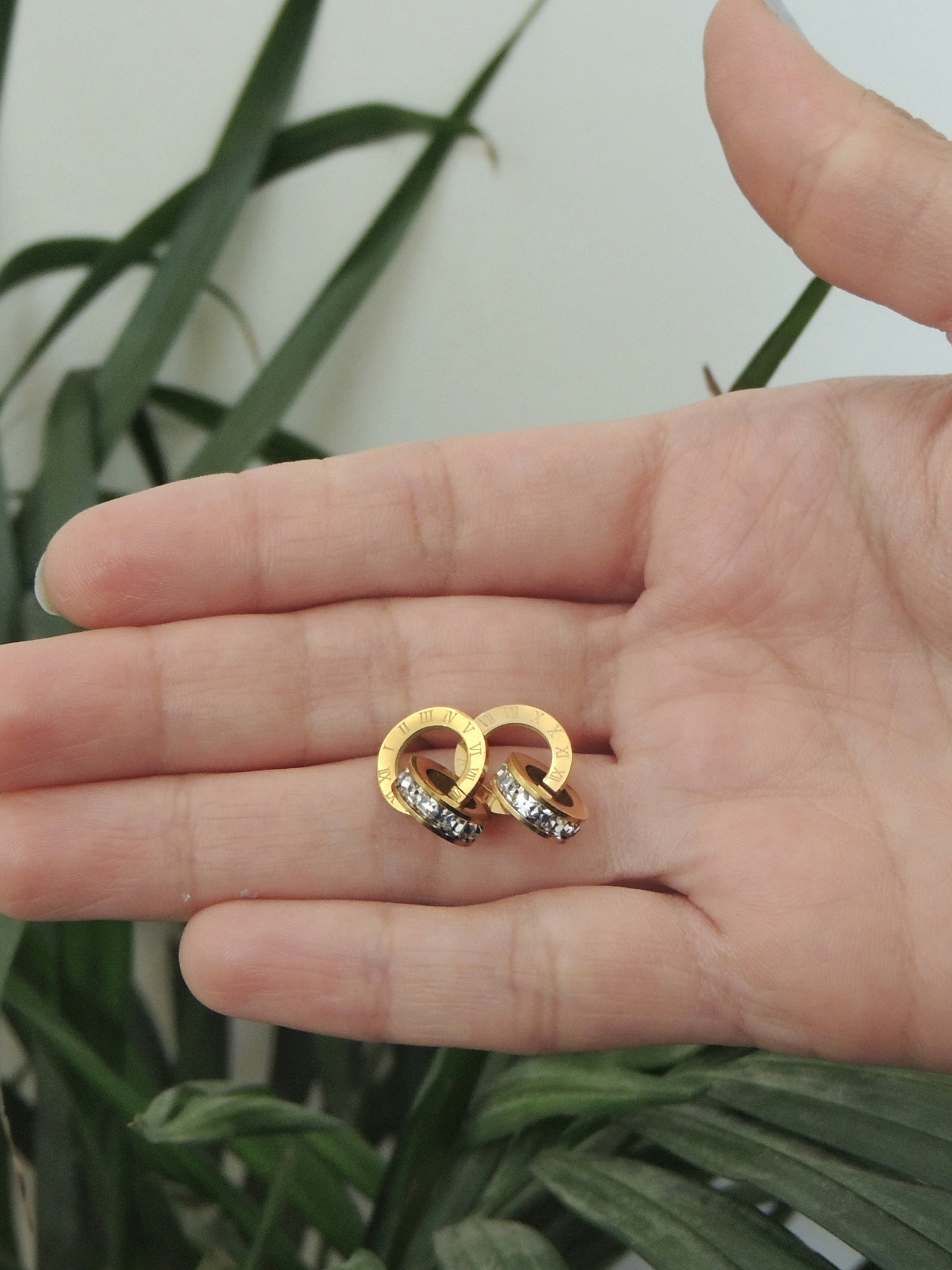 Close-up of gold Roman crystal earrings held in hand, highlighting shine and texture.