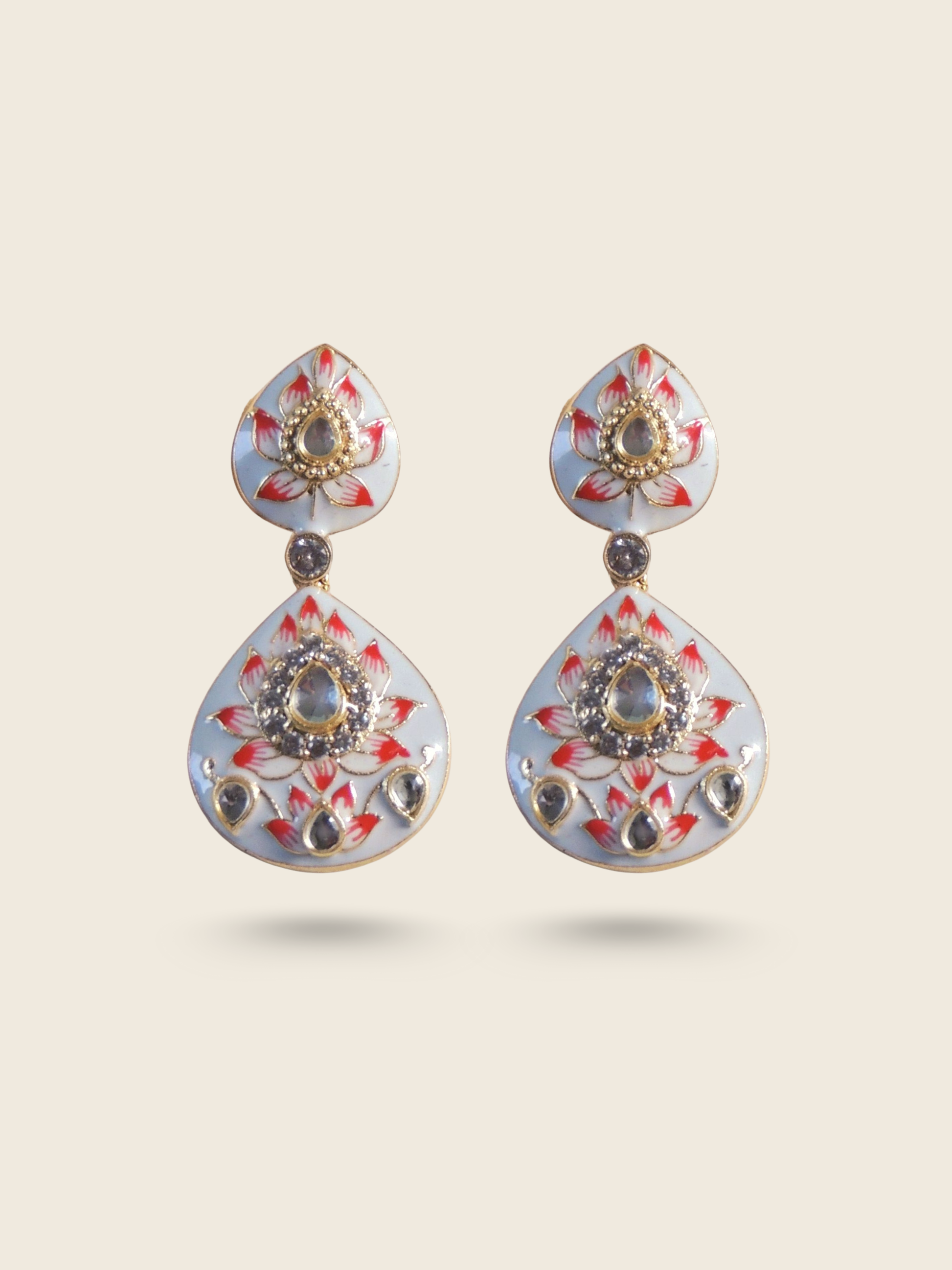 Traditional teardrop-shaped earrings with intricate red and white enamel work, adorned with embedded stones and floral motifs.