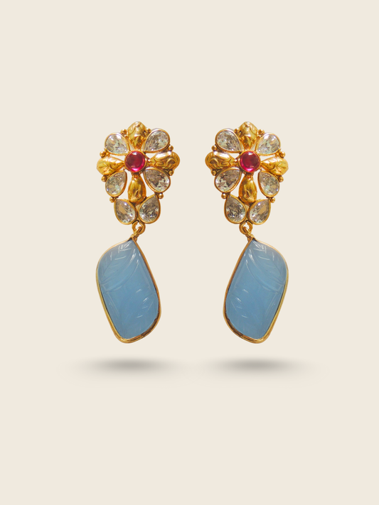 Floral-inspired gold earrings adorned with teardrop diamonds, a central ruby, and a large blue carved gemstone drop.